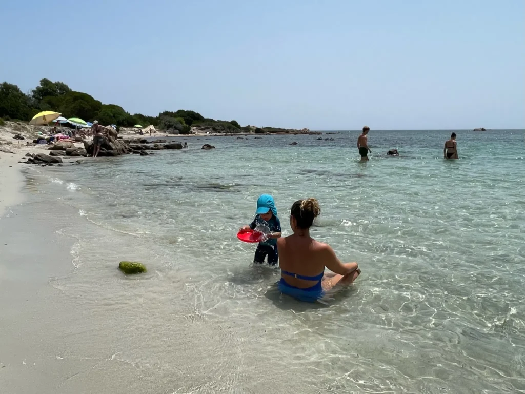 Niño pequeño con gorra en la playa de Cerdeña protegiéndose del sol veraniego, imprescindible con niños en verano