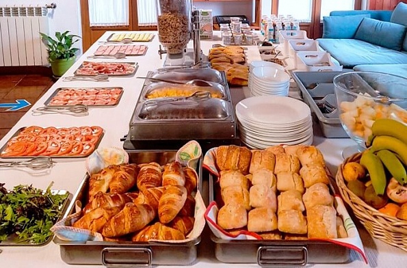 alt="Mesa larga con buffet completo de desayuno: croissants, fruta, embutidos y café en Russo Surfcamp"