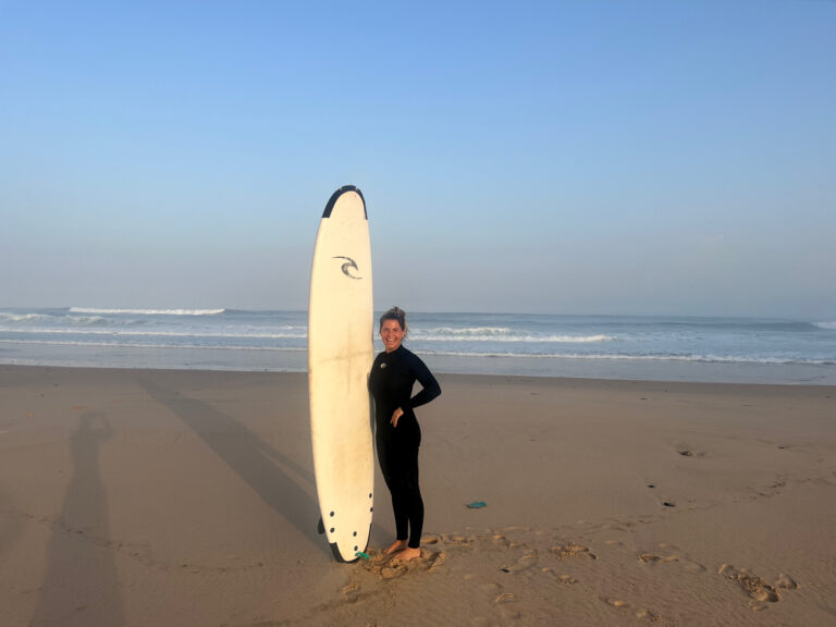 alt="Mujer posando con una tabla de surf larga en la playa de Vale Figueiras."