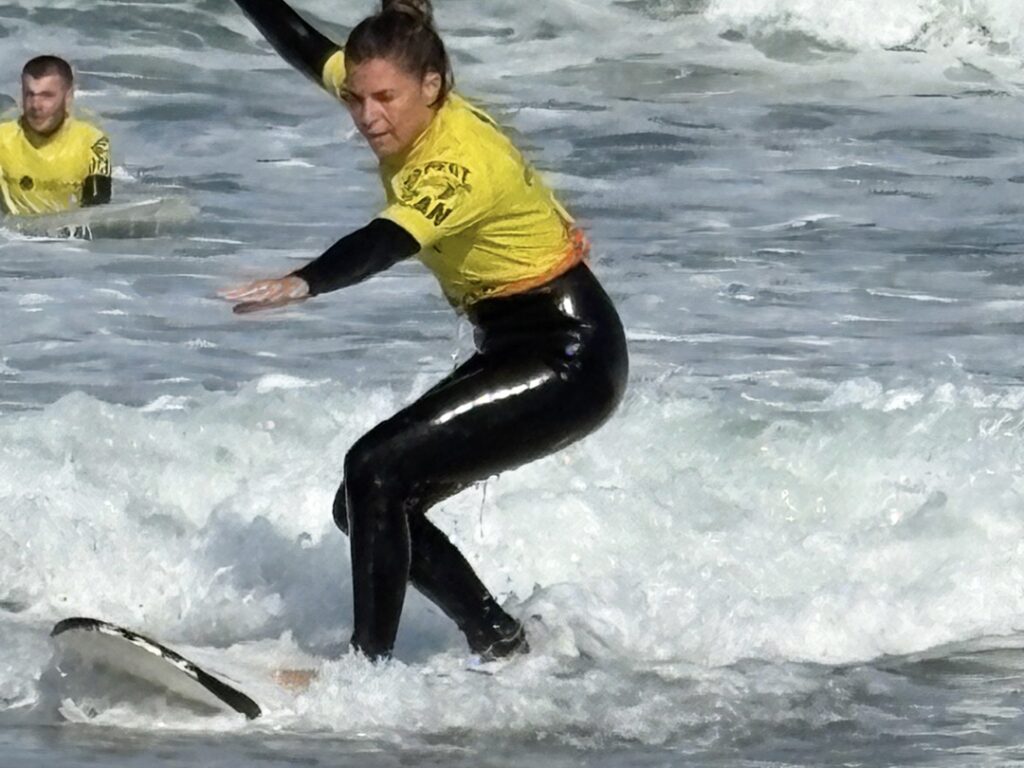 alt="Surfista con lycra amarilla de nivel principiante deslizándose en una ola en el Algarve"