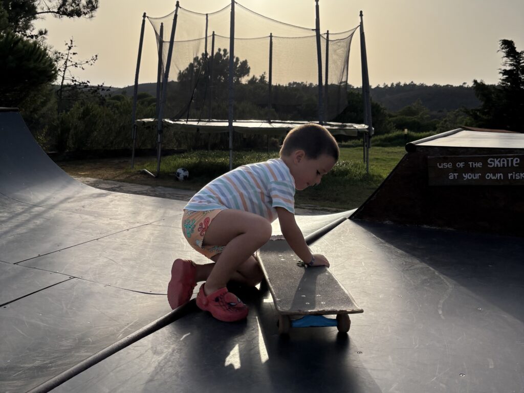 alt="Niño jugando con un monopatín en la rampa de skate del surfcamp al atardecer."