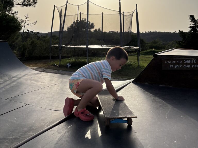 alt="Niño jugando con un monopatín en la rampa de skate del surfcamp al atardecer."