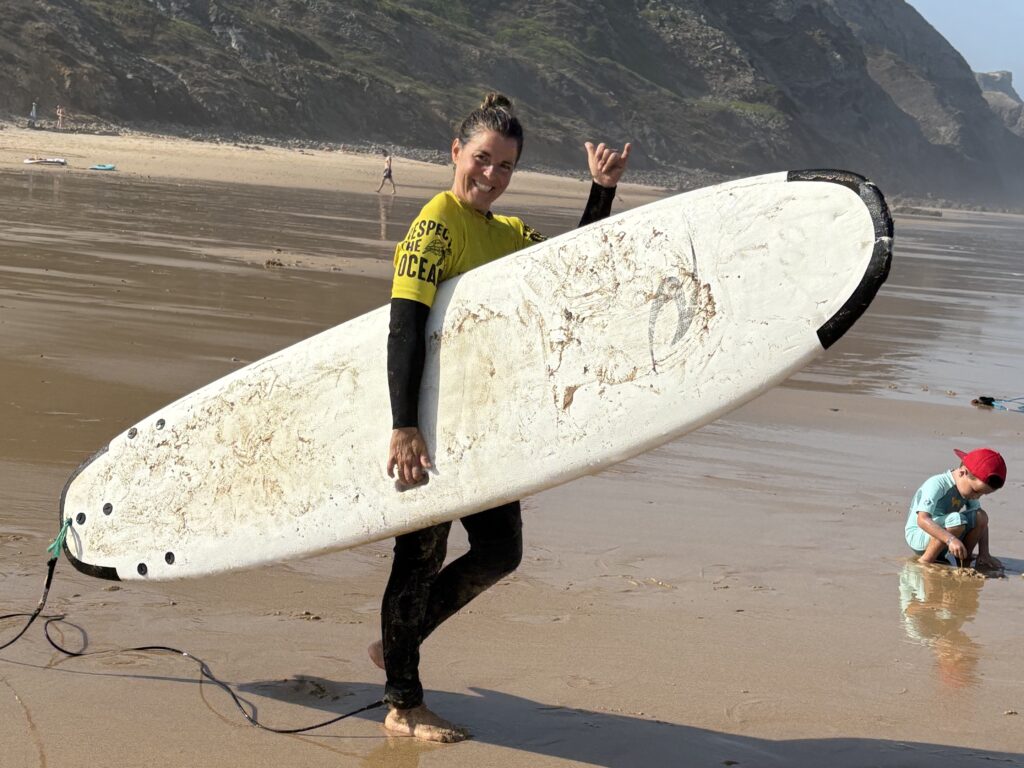 alt="Surfista sonriente con su tabla de surf en la mano en una playa portuguesa."