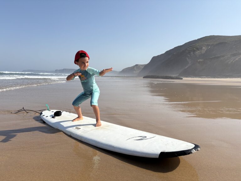 alt="Niño pequeño practicando el equilibrio sobre una tabla de surf en la orilla."