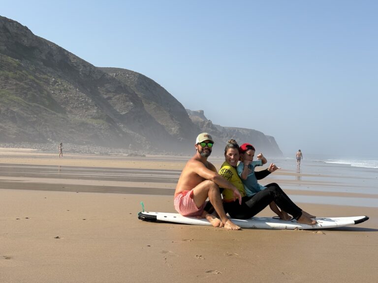 alt="Familia sentada sobre una tabla de surf de iniciación en la playa."