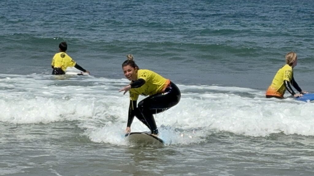 alt="Mujer con lycra amarilla de nivel intermedio cogiendo una ola con éxito en una playa del Algarve"