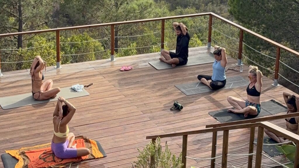alt="Clase de yoga grupal en plataforma de madera elevada en mitad de la naturaleza en Aljezur"
