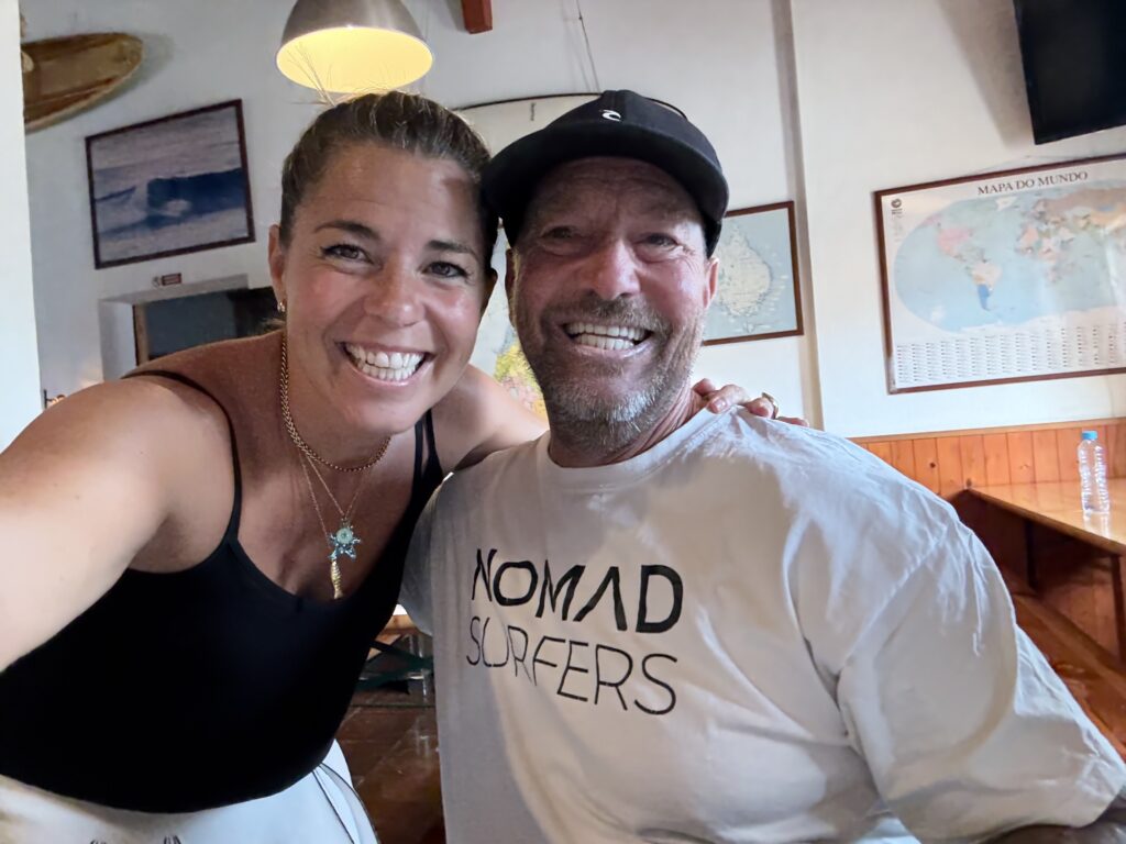 alt="Retrato cercano y sonriente de una huésped con Russo, el alma del surfcamp, en el salón social"