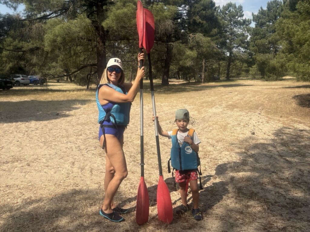 Madre e hijo posando con chalecos y remos rojos en una zona arenosa con pinos antes de empezar la actividad en las Hoces del Duratón con niños.