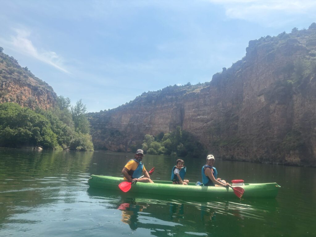 Familia de tres miembros remando junta en un kayak verde rodeada por los grandes cañones de las Hoces del Duratón con niños.